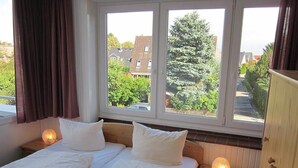 A double room with two beds, a window with a view of houses and trees, and bedside lamps. - Ferienwohnung in Westerland (Sylt)