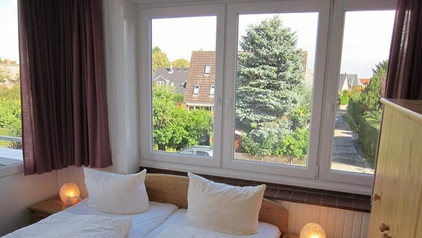 Une chambre double avec deux lits, une fenêtre donnant sur des maisons et des arbres, et des lampes de chevet.