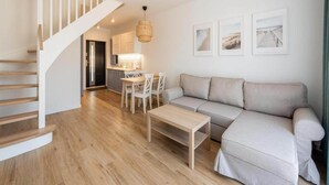 A modern living room with a wooden staircase, a dining area with a table and chairs, and a sofa. - Holiday Home Grzybowo Near Beach & Bike Path (Kolobrzeg)