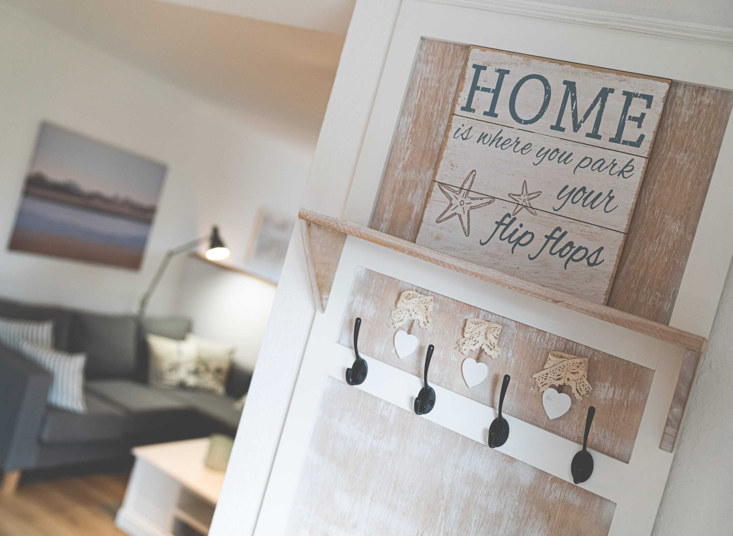 A wall-mounted sign with the text 'HOME is where you park your flip flops' and a wall-mounted rack with hooks and decorative items.