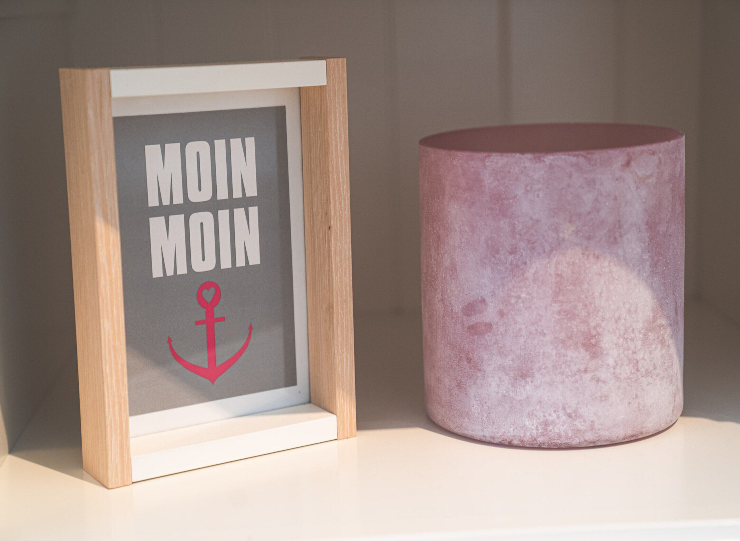 Een lijst met de tekst 'MOIN MOIN' en een rode anker, naast een roze, cilindrisch object.
