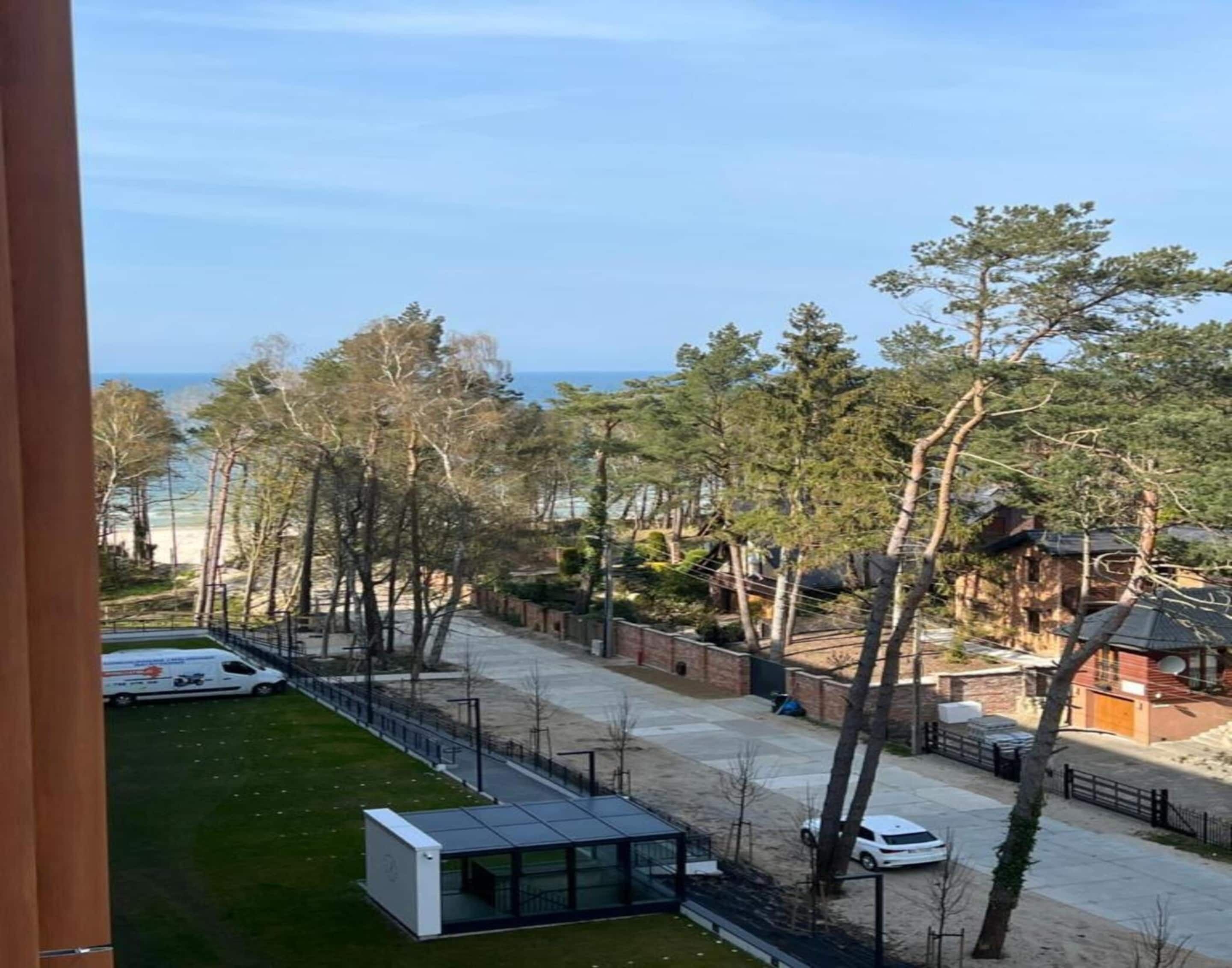 A view of a residential area with a modern building, trees, and a beach in the background.