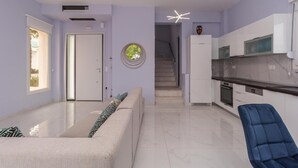 Ett modernt kök med vita skåp, en svart bänkskiva och en inbyggd ugn. Där finns en blå stol och en beige soffa med mönstrade kuddar.