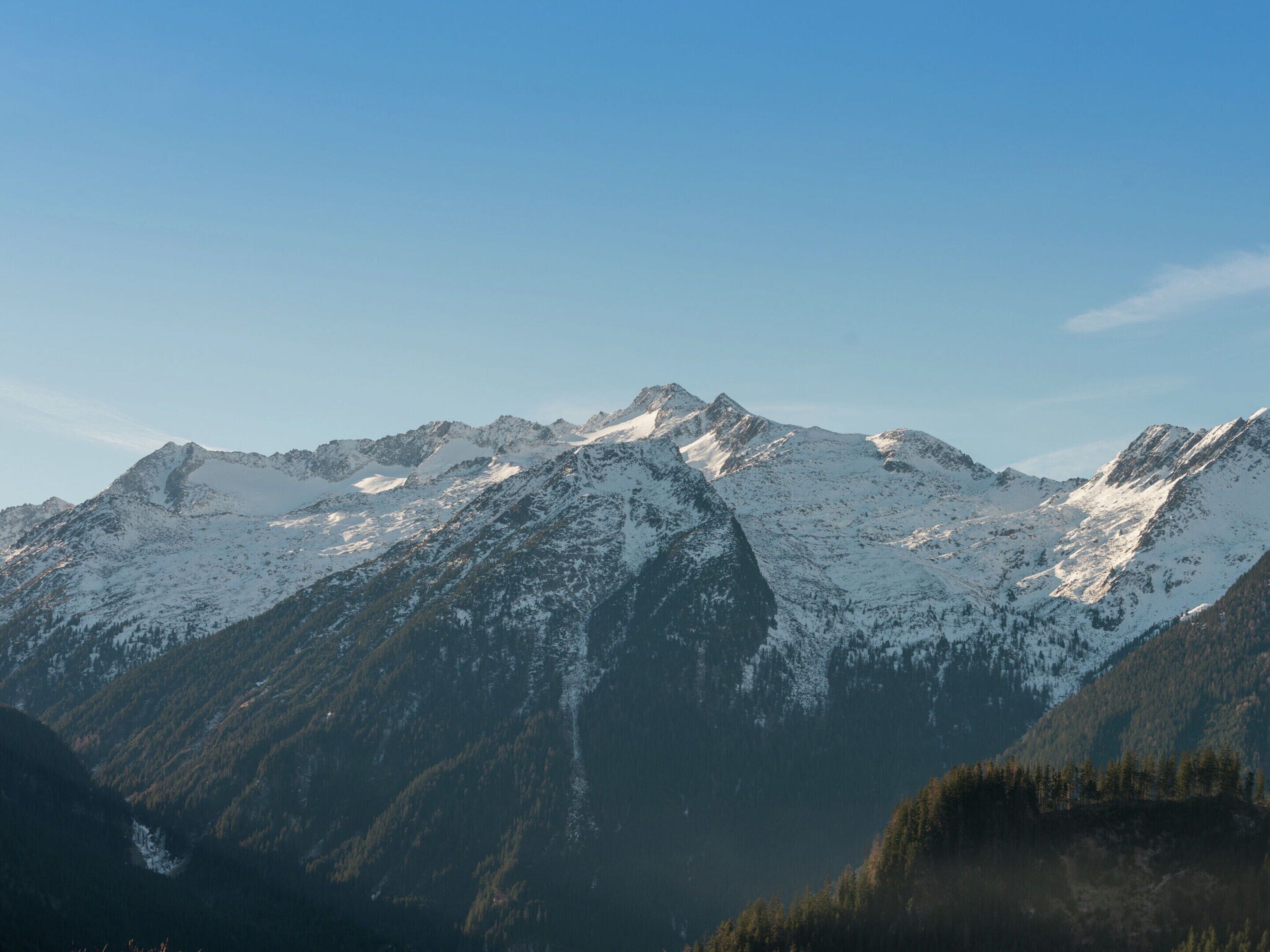 A mountain landscape with snow-covered peaks and dense forested areas.
