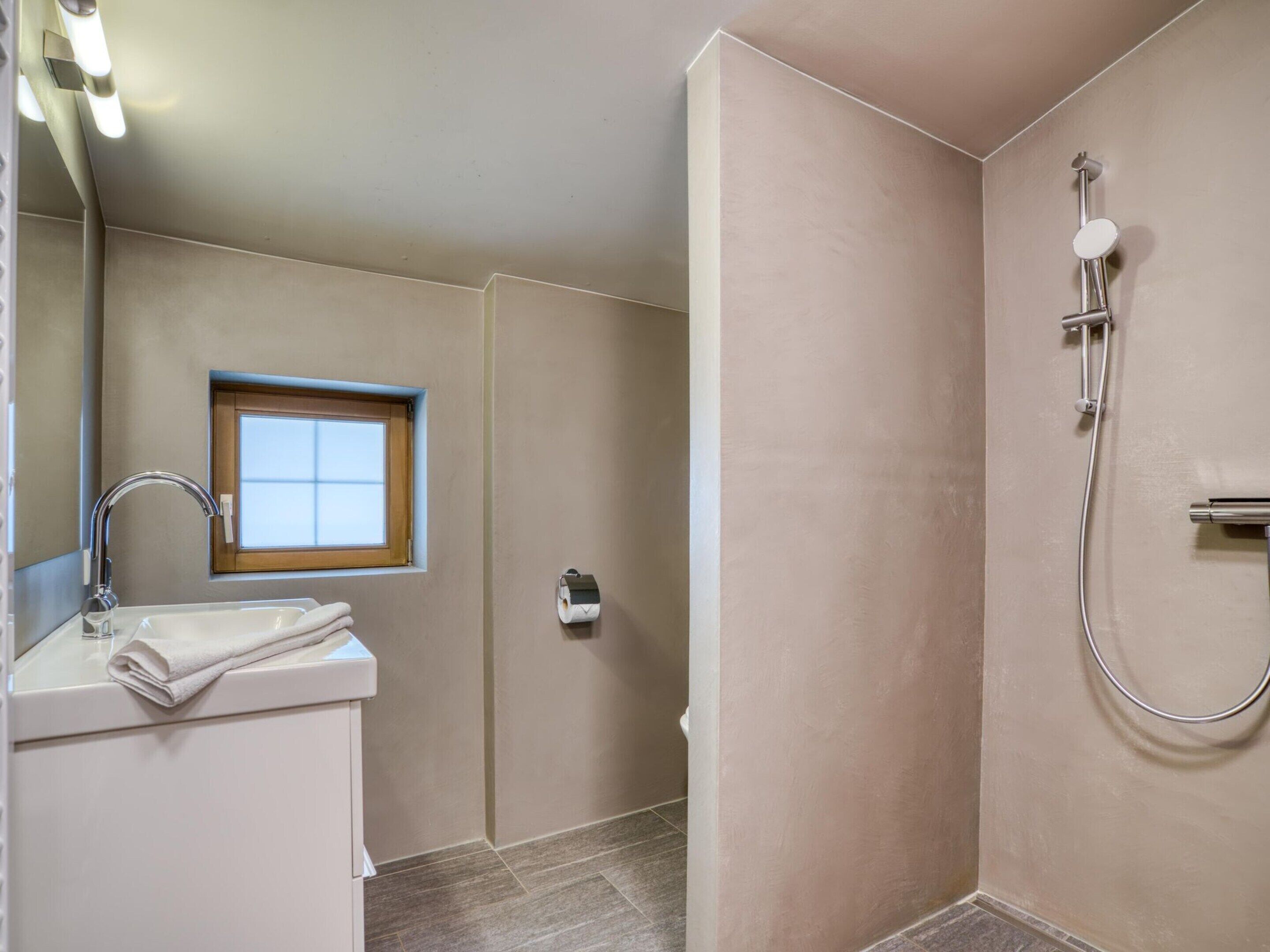 A bathroom with a sink, mirror, window, and shower.