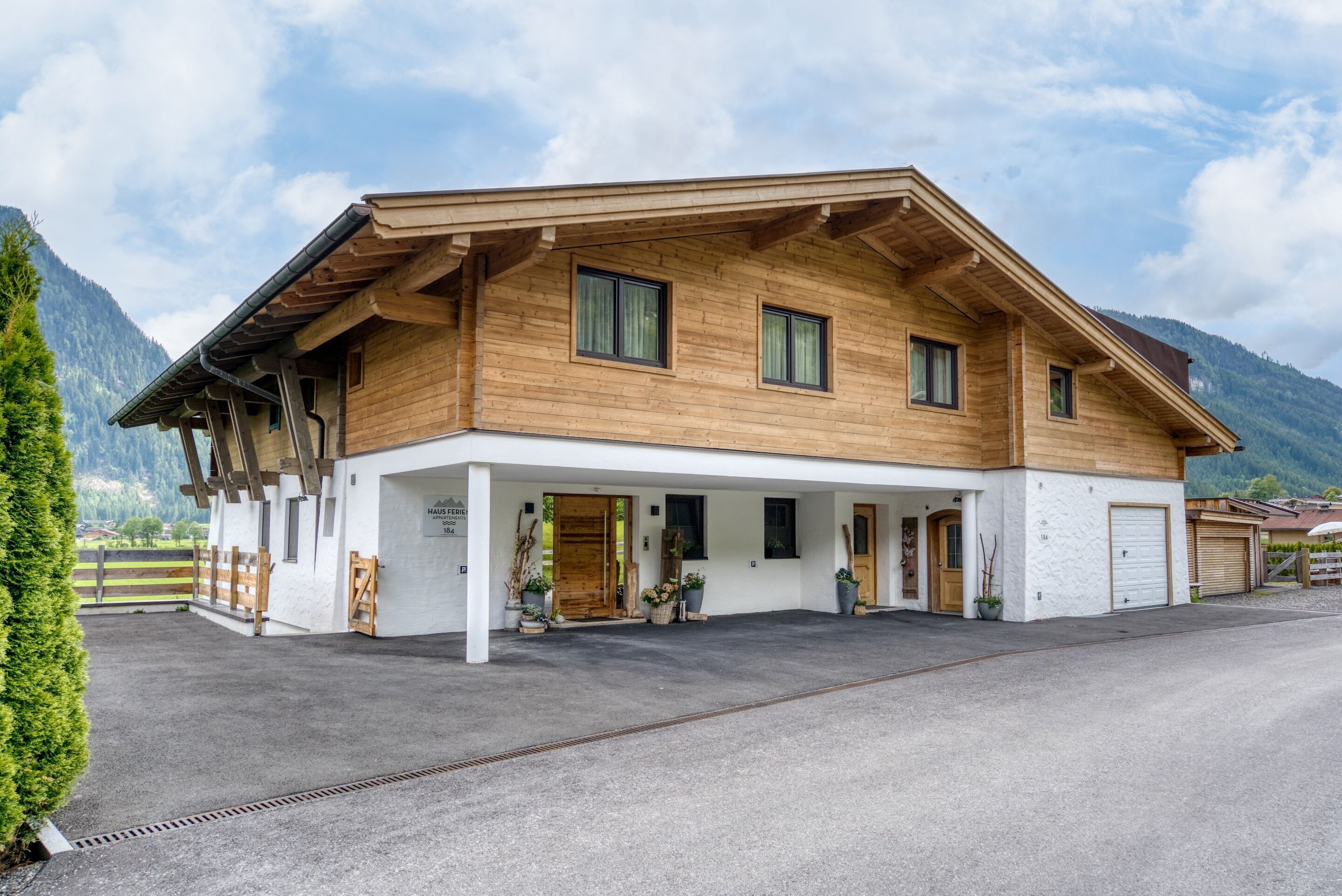 Une maison en bois à deux étages, dotée d’un porche couvert, d’un garage et surplombant un paysage montagneux.