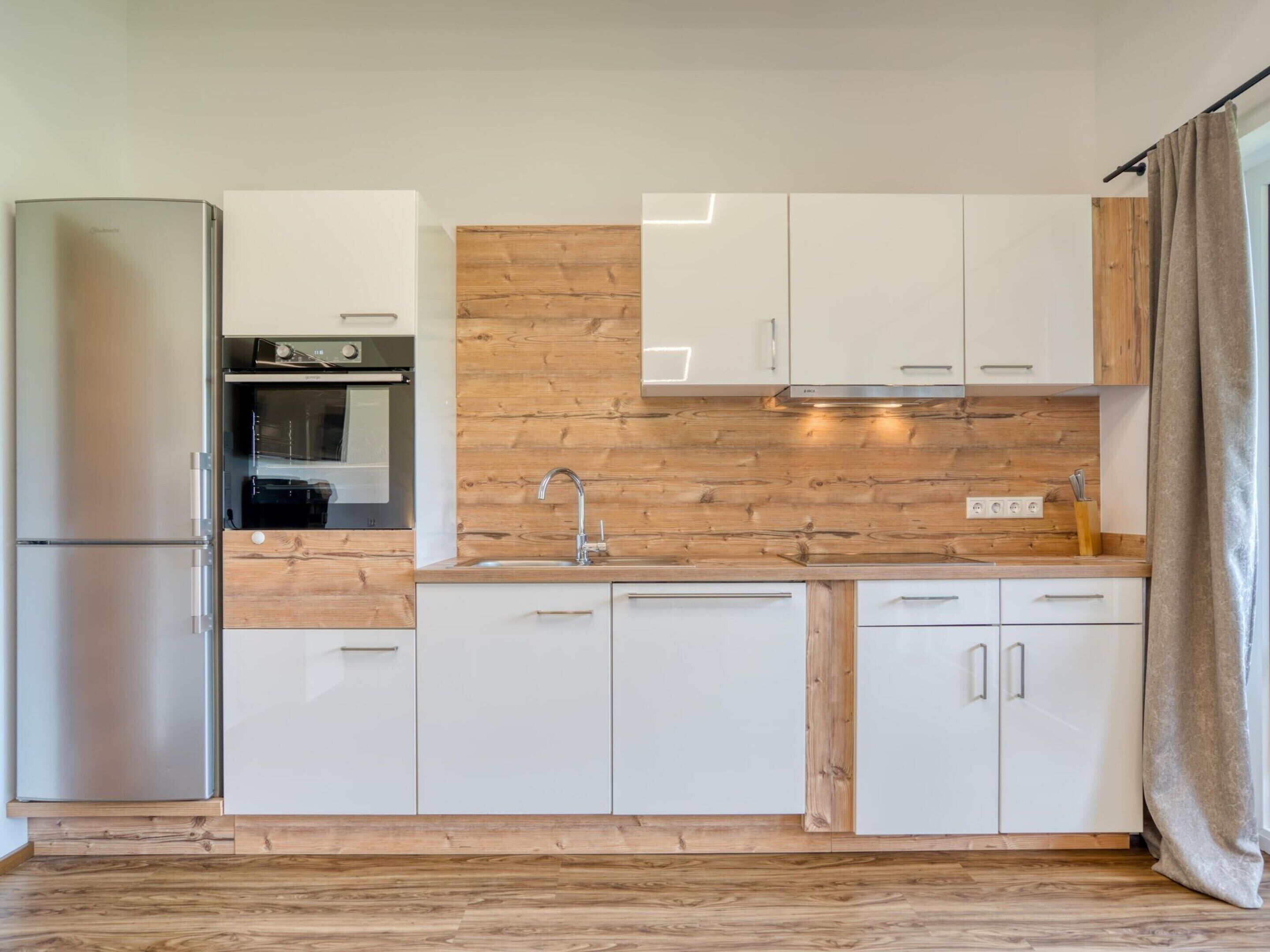 Eine moderne Küche mit weißen Schränken, einem Edelstahlkühlschrank, einer Holzrückwand und einem eingebauten Ofen.