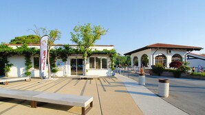 A building with a white facade, large windows, and a tiled roof. There is a bench in the foreground and a tree in the background. - Bungalow in Caorle With Garden Furniture (Caorle)