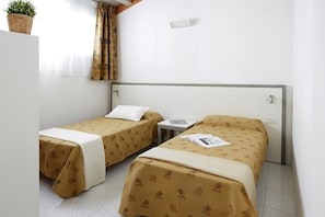 Ein Hotelzimmer mit zwei Einzelbetten, einem kleinen Tisch und einem Fenster mit Vorhängen.