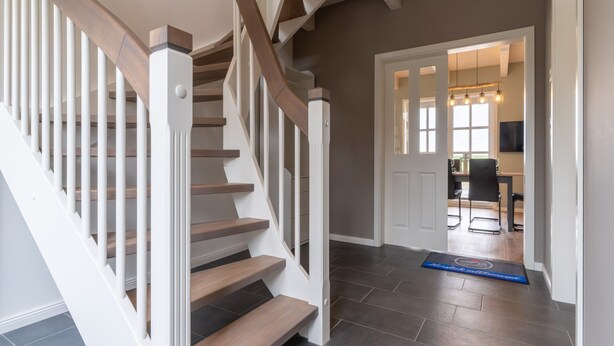 Eine Treppe mit Holzboden und weißen Geländern, die zu einem Raum mit Essbereich führt.