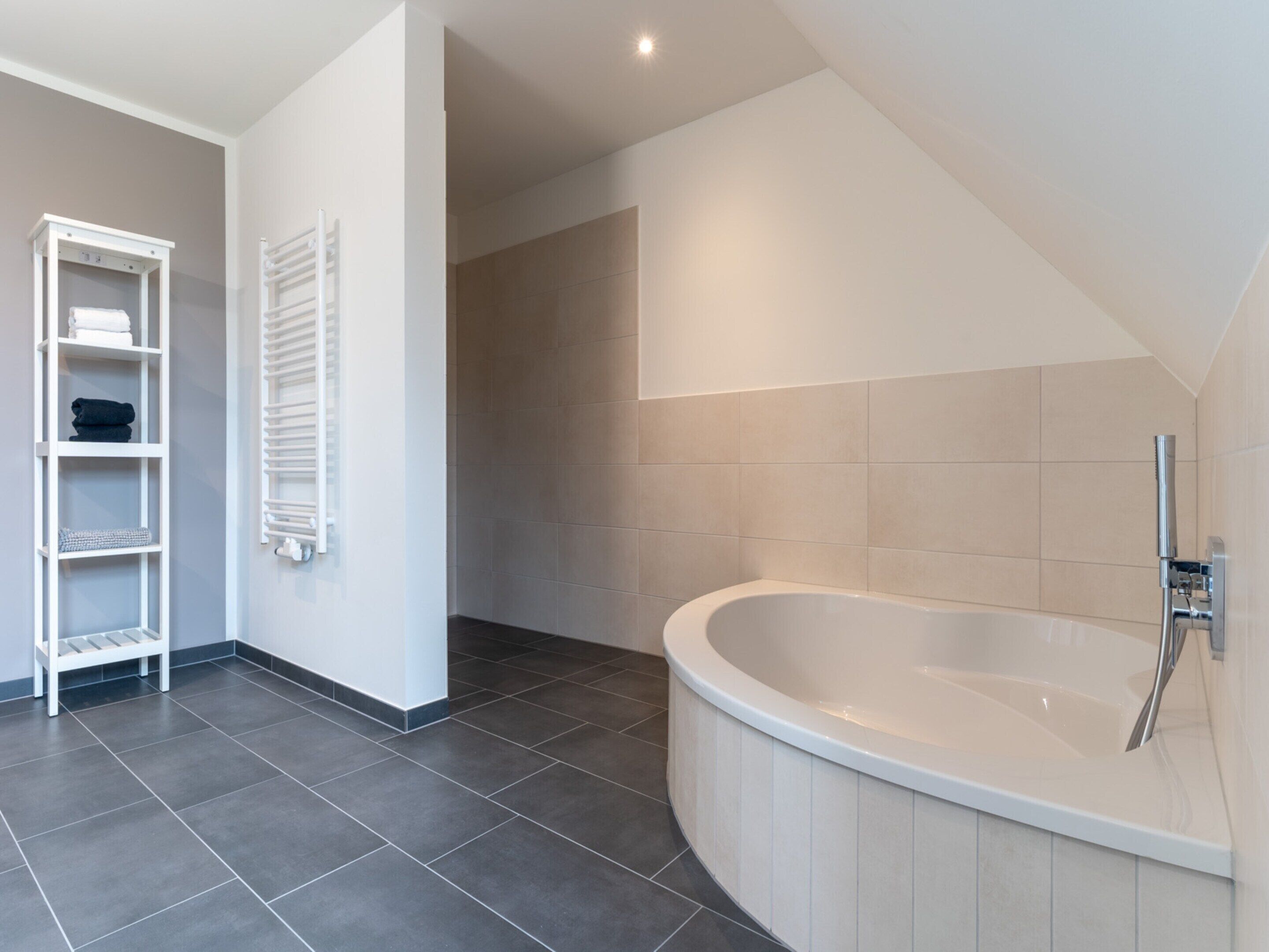 A modern bathroom with a freestanding bathtub, a white towel rack, and a built-in shelf unit.