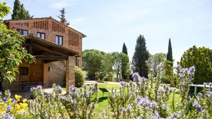 A rustic brick building with a covered patio area, surrounded by a well-maintained garden with various flowering plants. - Apartment in Montaione With Carport (Montalcino)