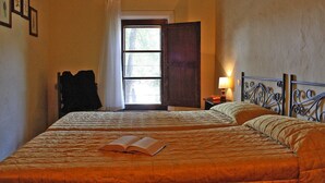 A bedroom with two beds, a window with curtains, a bedside table with a lamp, and a coat rack. - Apartment in Montaione With Carport (Montalcino)
