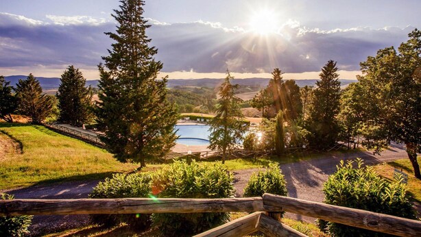 A scenic view of a mountainous area with a swimming pool, surrounded by trees and a wooden fence. - Apartment in Montaione With Carport (Montalcino)