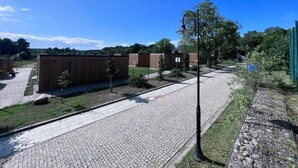 A paved walkway with wooden buildings, a lamp post, and a fenced area with trees. - Holiday Homes With Sauna and Jacuzzi in Trzesacz-formerly TUI Ferienhaus (Rewal)