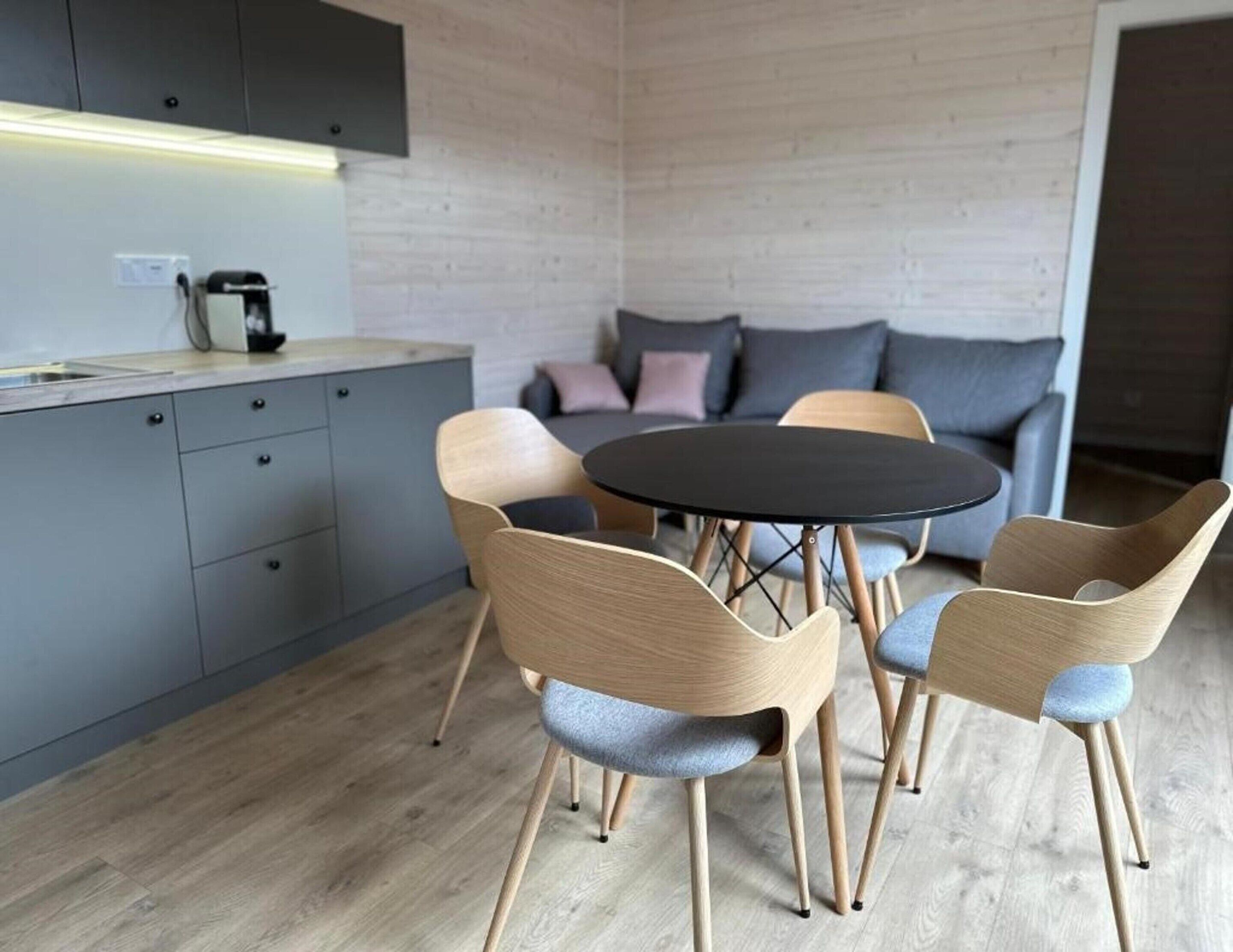 A modern kitchen with grey cabinets, a round table, and four chairs with light wood frames and grey cushions.