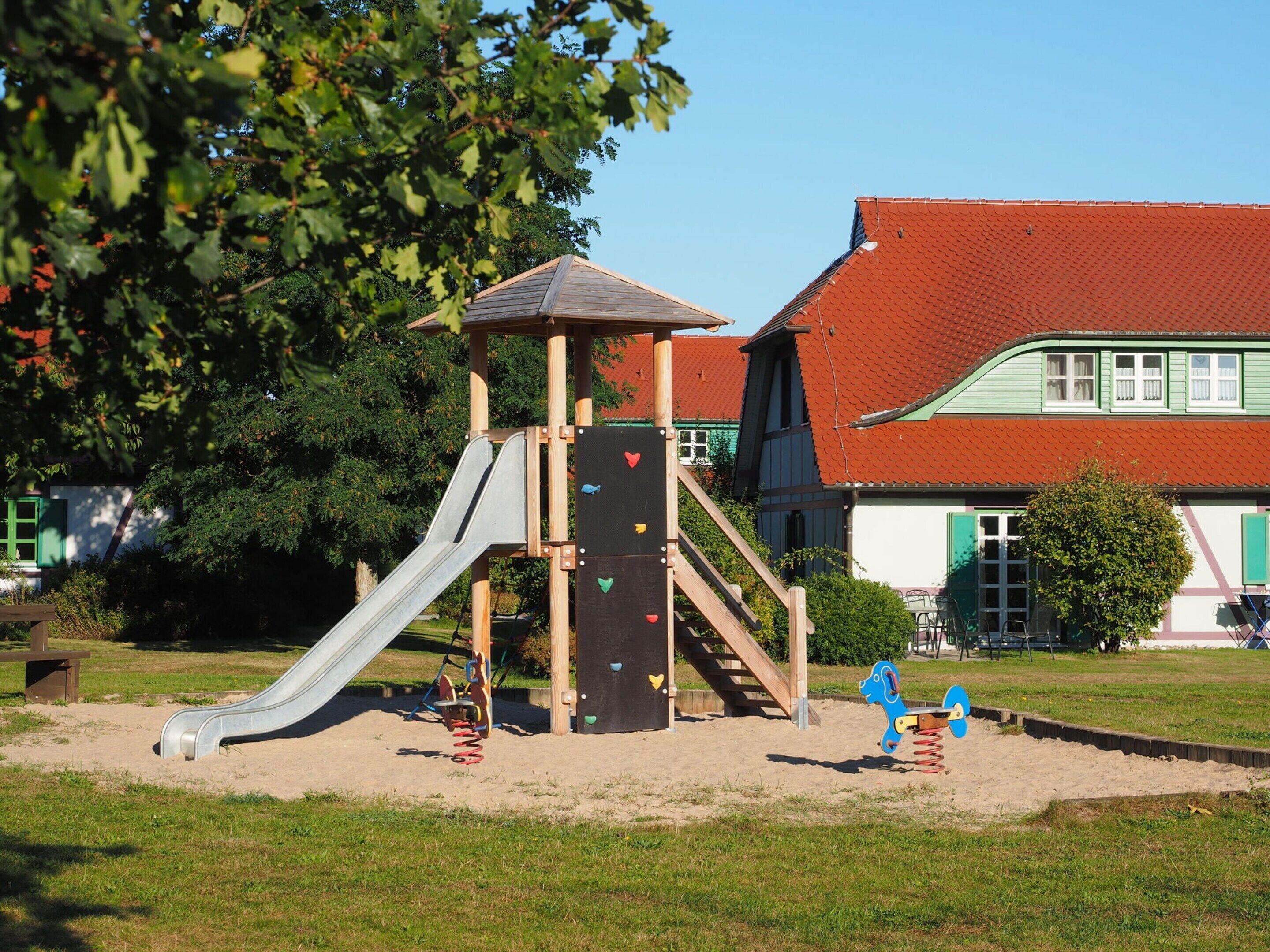 Ein Spielplatz mit Rutsche, Kletterwand und Schaukeln.