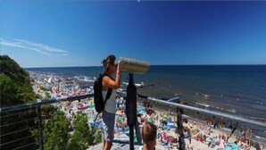 A woman and a child using binoculars overlooking a crowded beach with umbrellas and people. - Comfortable, 2-person Holiday Studio (Ustronie Morskie)
