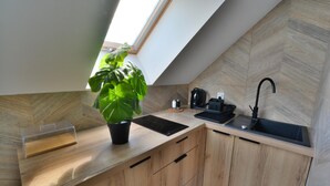 A modern kitchen with a skylight, wooden cabinetry, a black sink, and a coffee maker. - Comfortable, 2-person Holiday Studio (Ustronie Morskie)