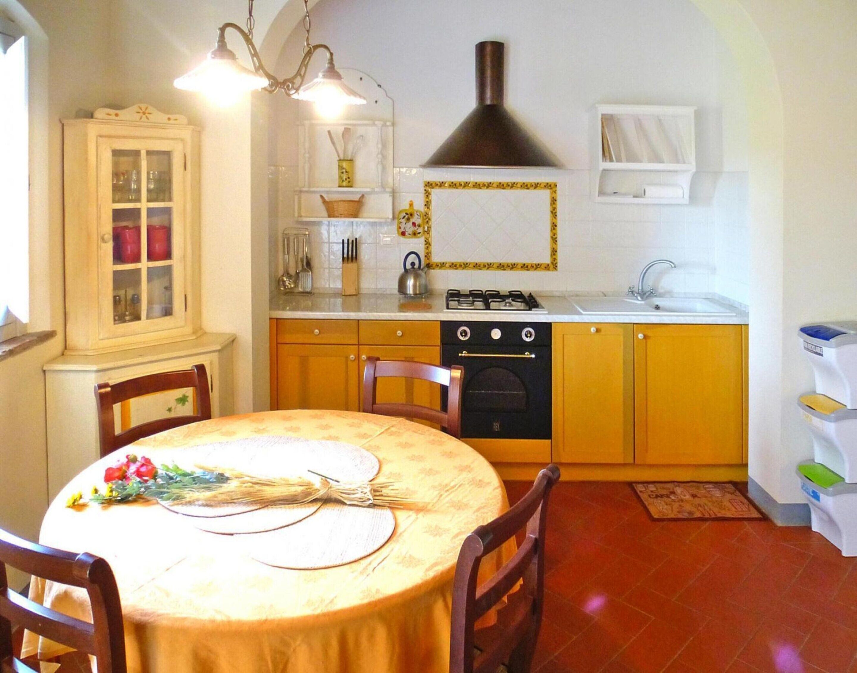 Une cuisine compacte équipée d’une cuisinière, d’un four et d’un évier. On y trouve une table à manger avec des chaises et un meuble avec des portes en verre.