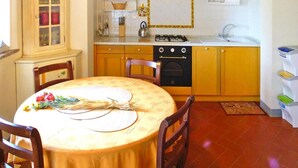 Una cucina funzionale con piano cottura, forno e lavello. C'è un tavolo da pranzo con sedie e un pensile con ante in vetro.