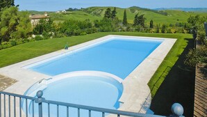 Una piscina rettangolare con bordo circostante, con vista su dolci colline e vegetazione.