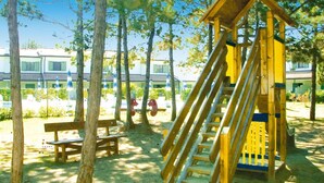 Une aire de jeux avec un toboggan en bois et une structure d’escalade, entourée d’arbres et de bancs.