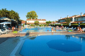A swimming pool with multiple lanes, surrounded by lounge chairs and umbrellas. - Terraced House Bibione Near Sandy Beach (San Michele al Tagliamento)