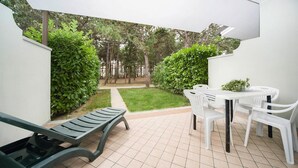 Une terrasse avec un fauteuil de jardin vert, une table blanche avec des chaises et un sol carrelé.