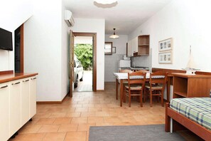 A compact room with a bed, a dining table with chairs, a kitchenette, and a TV on the wall. - Terraced House Bibione Near Sandy Beach (San Michele al Tagliamento)