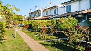 Une rangée de maisons blanches aux toits recouverts de tuiles rouges, un sentier bordé de gazon et des arbustes en fleurs.