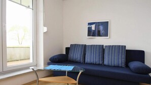 Olohuoneessa on tummansininen sohva, raidalliset koristetyynyt, lasinen sohvapöytä ja seinällä oleva kehystetty taulu.