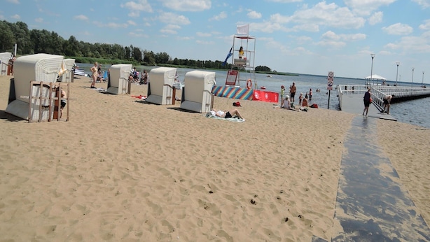 Ein Strand mit Liegestühlen, einem Rettungsturm und einem Steg.
