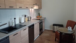 Eine moderne Küche mit hellen Holzschränken, Edelstahlgeräten und einer kleinen Essecke mit einem Korbstuhl.