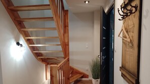 Eine Holztreppe führt zu einer Zwischenebene, einer schwarzen Tür mit Glasfenster und einer an der Wand befestigten Pflanze.