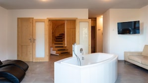 Una sala de estar moderna con una bañera blanca grande, un sofá color beige y una escalera de madera que sube a un segundo piso.