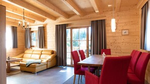Un interior de madera con un sofá, sillas rojas, una mesa de comedor y una araña.