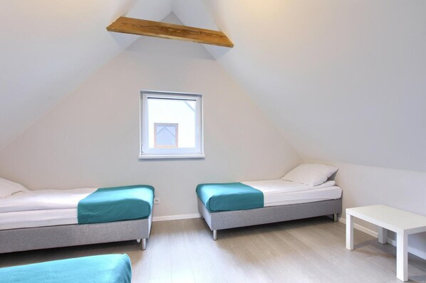 Una habitación pequeña y luminosa con dos camas individuales, una mesita y un ventanal.