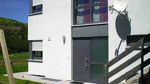 A modern two-story building with a grey door and windows, a satellite dish, and a wooden staircase. - Modern Flat in Messstetten Town (Messstetten)