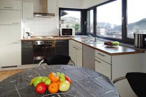 A modern kitchen with a microwave, stove, and sink. A fruit bowl is on the table, and there's a window with a view of the outdoors. - Modern Flat in Messstetten Town (Messstetten)