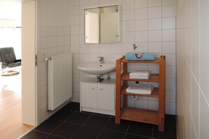 A bathroom with a white sink, a mirror, and a wooden shelf with towels. - Modern Flat in Messstetten Town (Messstetten)