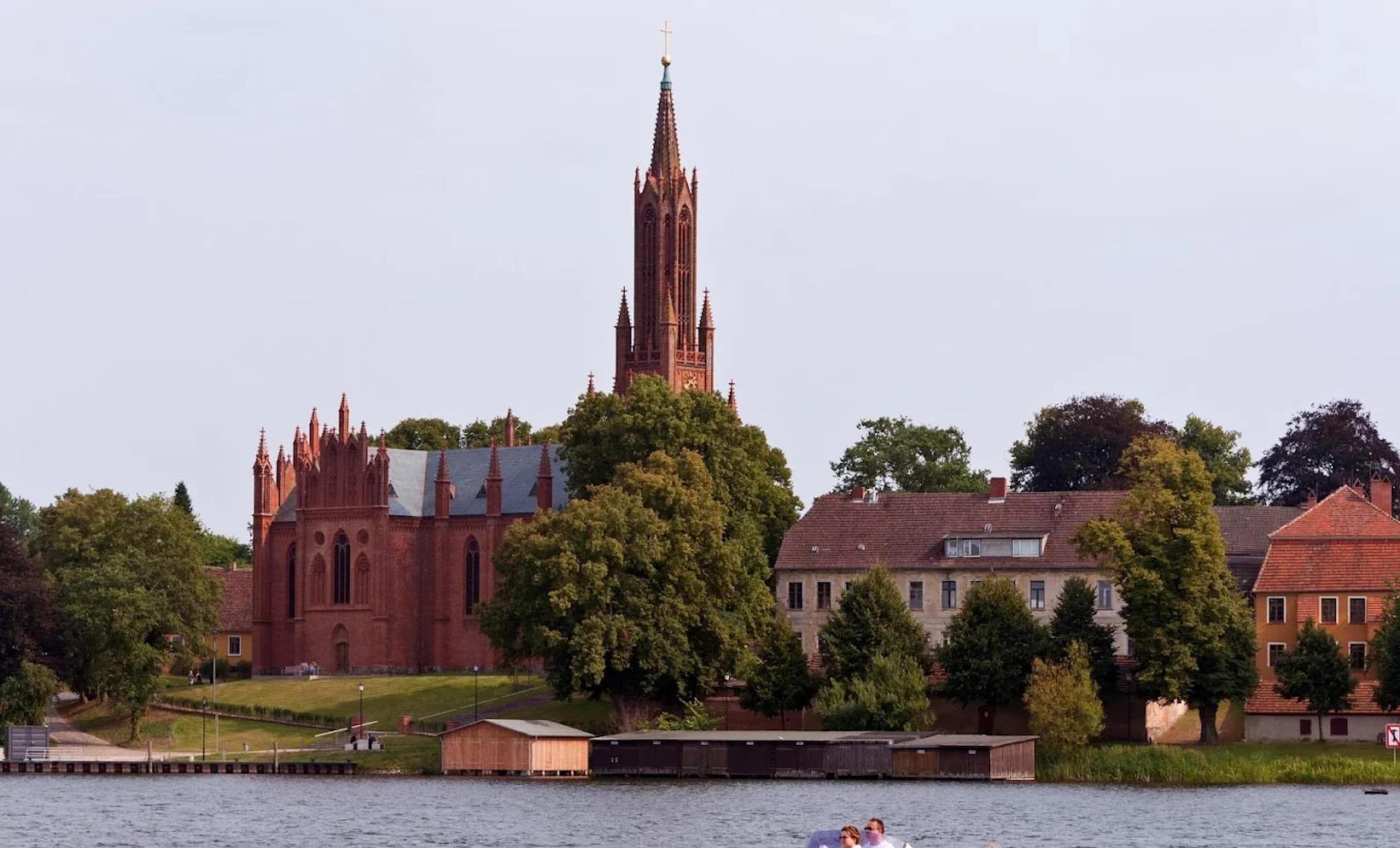 Une église dotée d’un flèche haute et d’une étendue d’eau au premier plan.