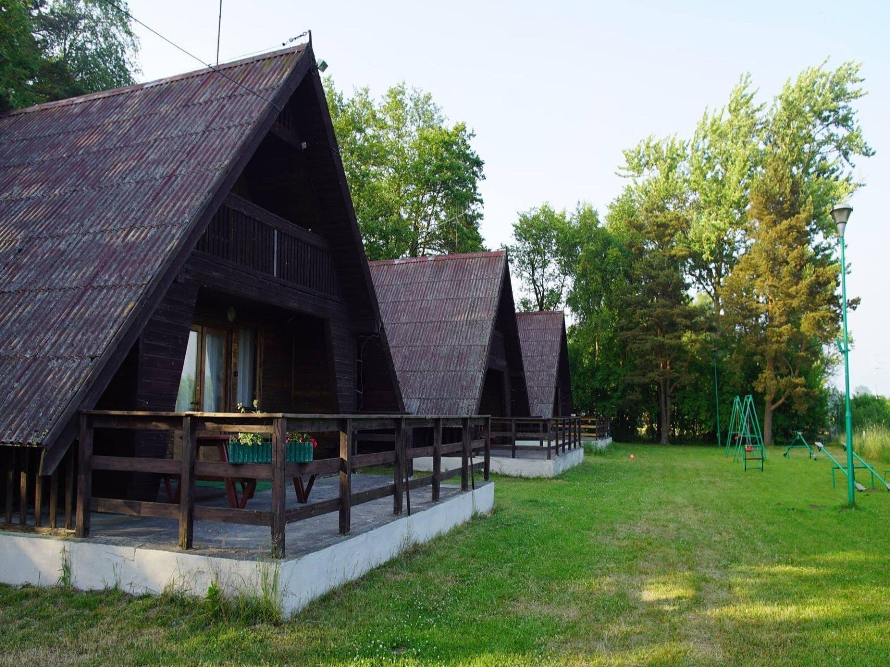 Eine Reihe von Holzhütten mit Satteldächern, eine Holzterrasse und ein Spielplatz im Hintergrund.