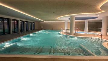 Una piscina interior con agua cristalina, rodeada por un muelle de madera y paredes de vidrio.