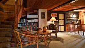 A cozy log cabin interior with a staircase, a sofa, two chairs, a table, a lamp, and a bookshelf. - Farmhouse Near Afritzer See & Nockberge Trails (Treffen)