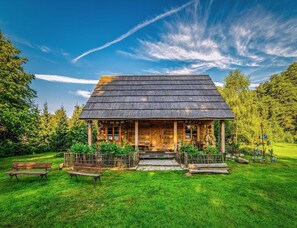 A wooden cabin with a thatched roof, surrounded by a well-maintained lawn and trees. - Holiday Home in Belczna Near Lake and Forests (Łobez)