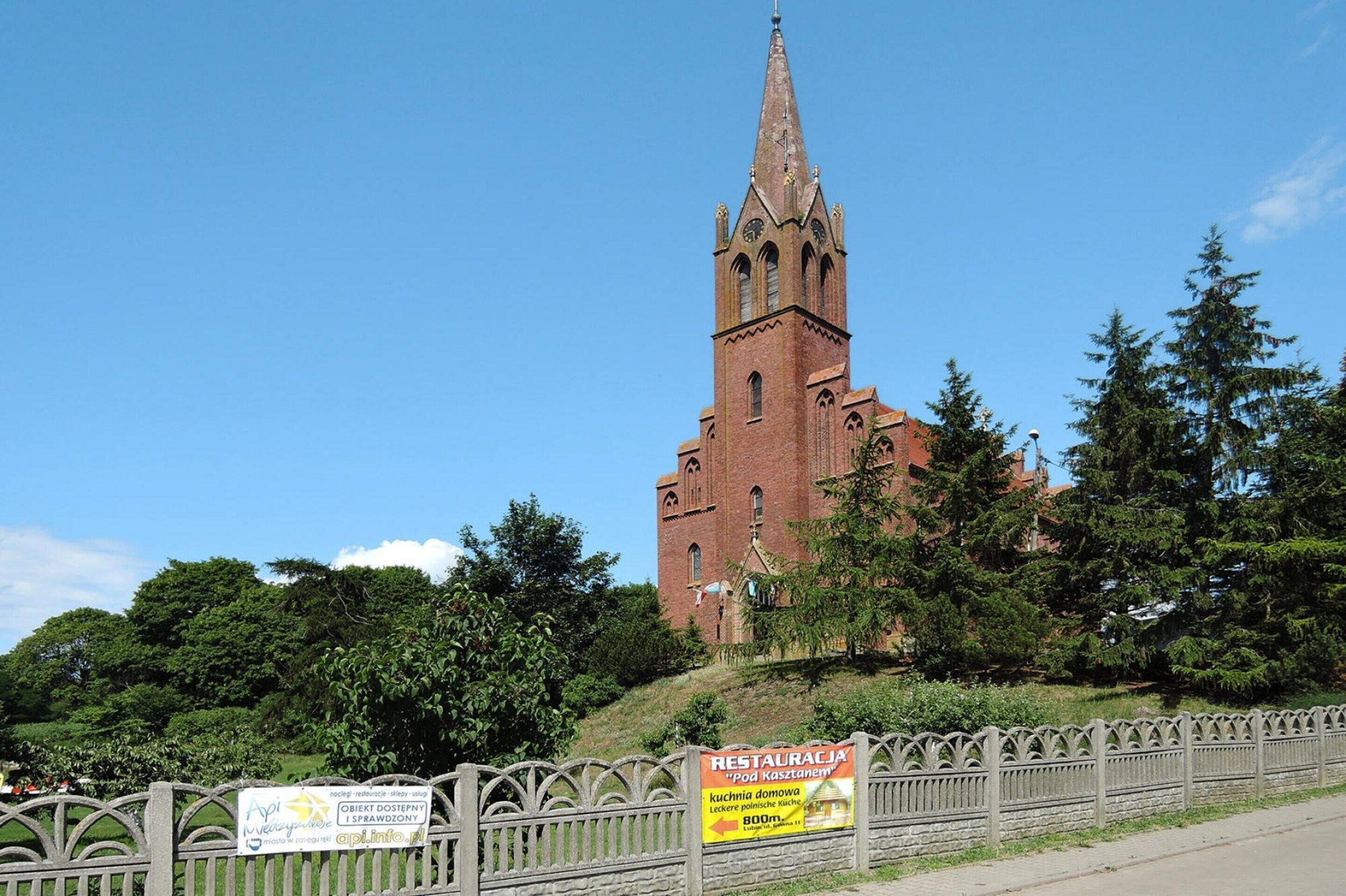 A church with a tall spire and a signboard in front.