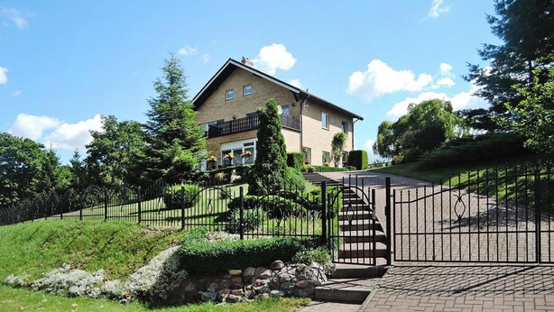 A two-story house with a balcony, surrounded by a well-maintained garden and a metal gate. - Holiday Home in Lubin Near Wollin Park (Międzyzdroje)
