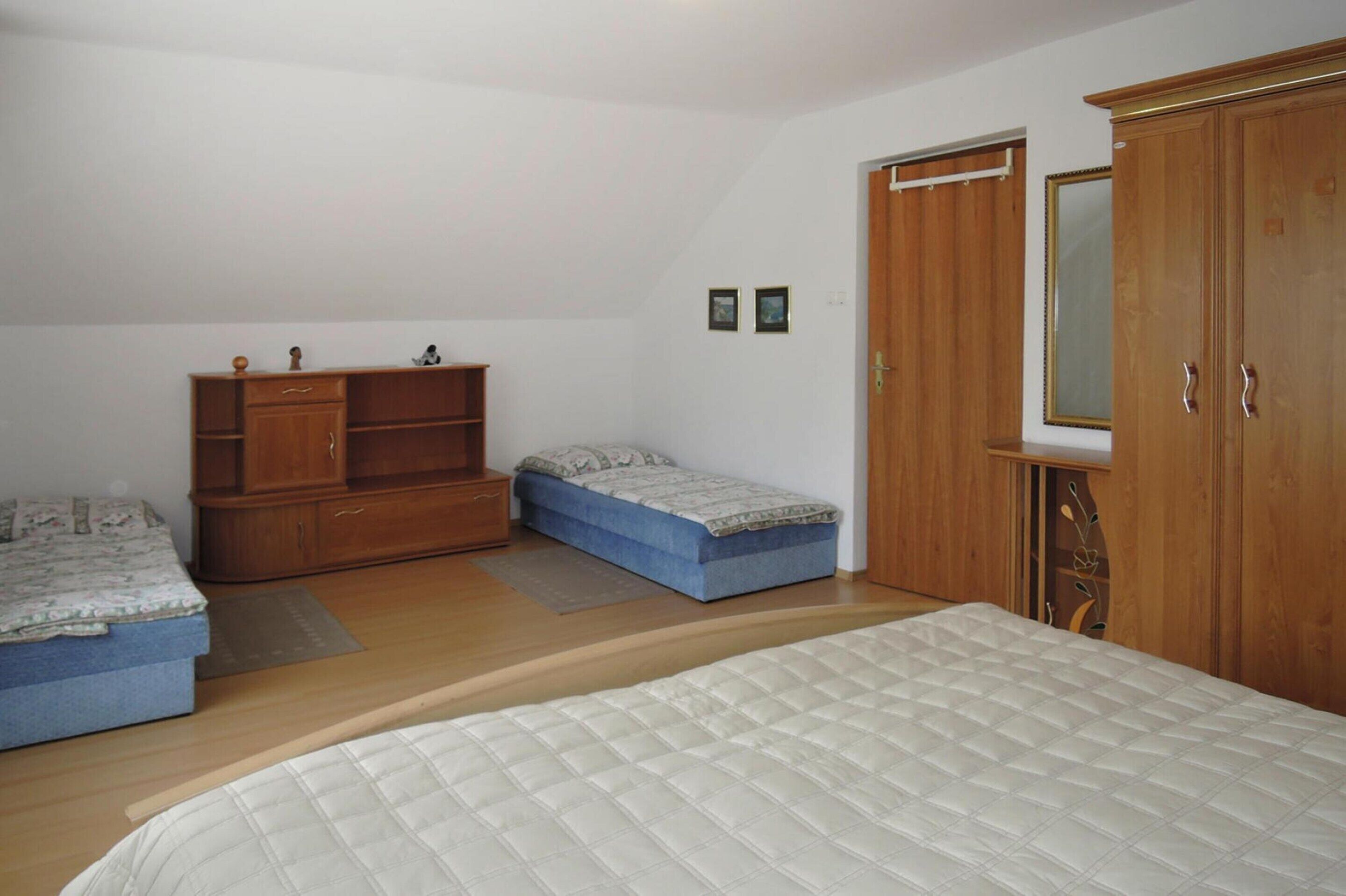 Une chambre à coucher avec un grand lit, deux petits lits, une armoire en bois et un petit meuble.
