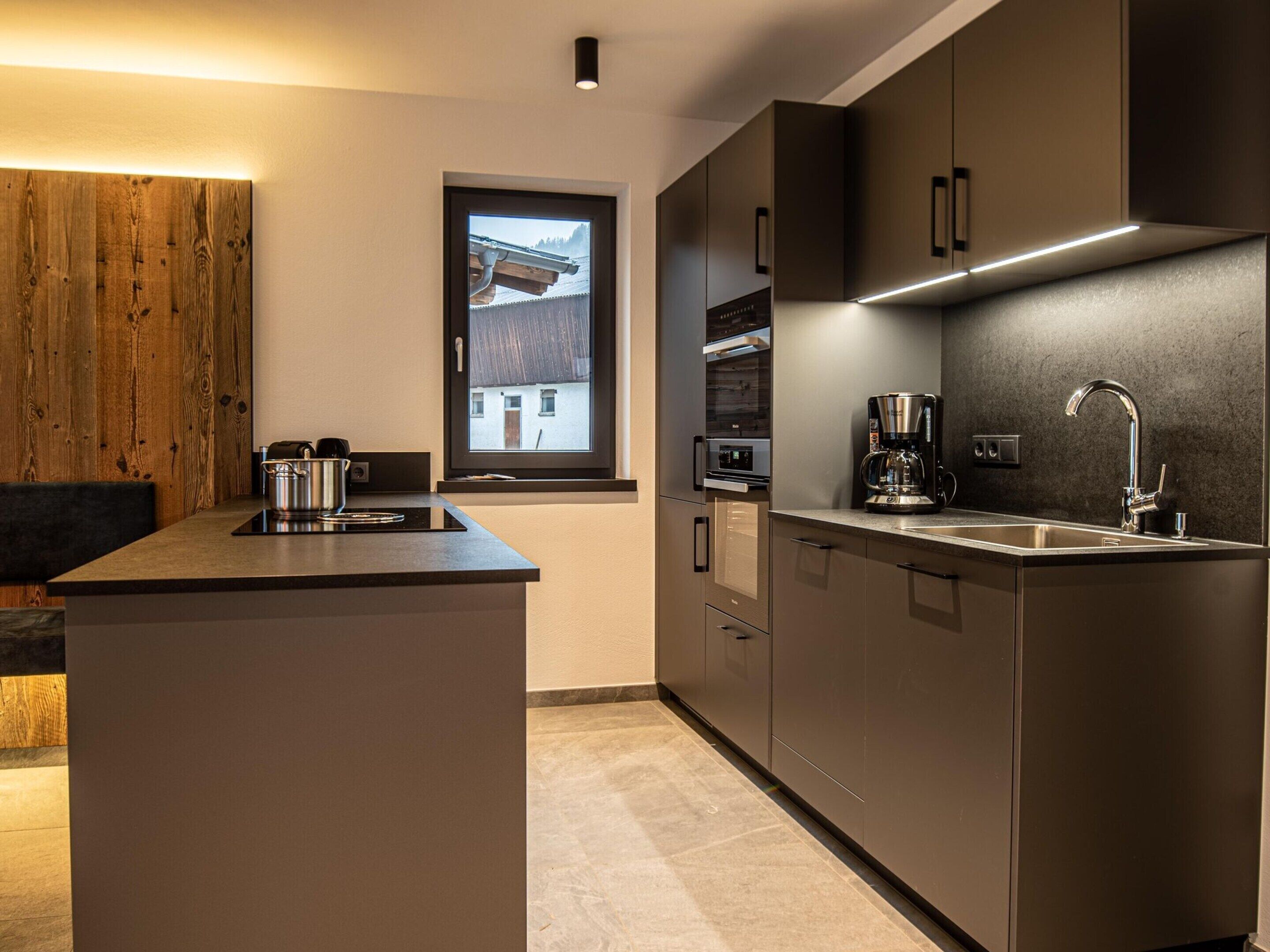 A modern kitchen with a central island, stainless steel appliances, and a window with a view of a house.